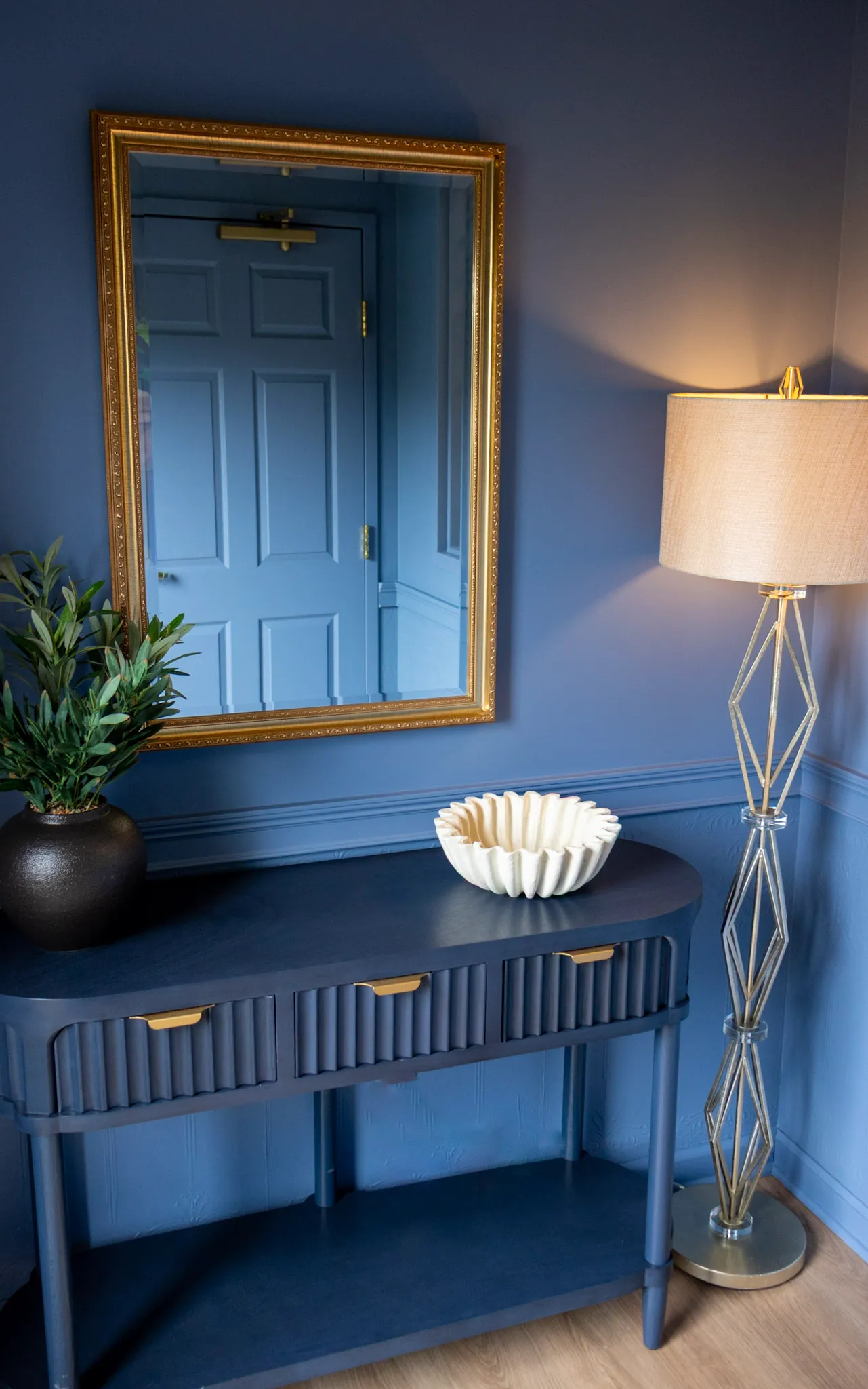 An office mirror above a console table beside a lamp